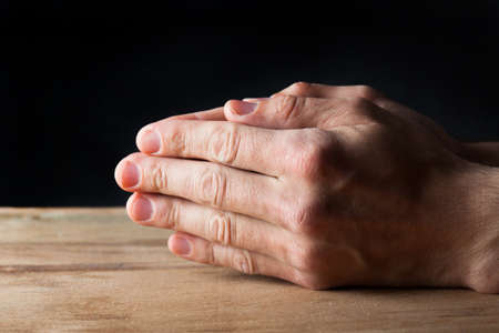 Hands of praying young man on a wooden desk background.の写真素材