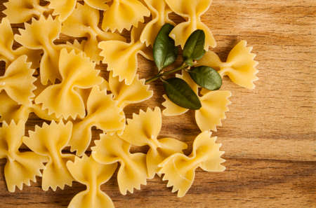 Italian cuisine concept - Wholemeal farfalle pasta in wooden spoon with fresh basil and tomatoes od dark rustic wooden background . With copy space for your textの写真素材