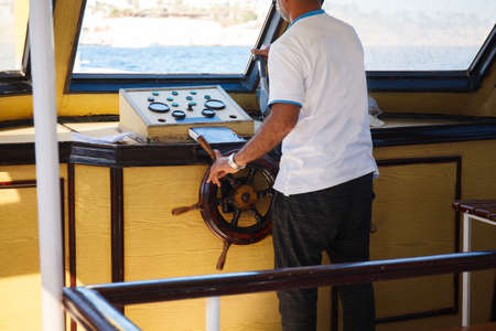 close up of senior man steering wheel and navigating sail boat or yacht floating in sea. travel and people conceptの写真素材