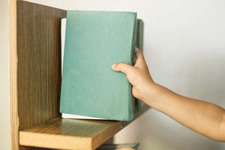 Male hand choosing and picking white book on wooden bookshelf in public library.の写真素材