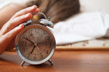 Young sleeping woman and alarm clock in bedroom at home