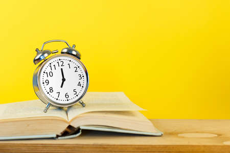 Silver vintage alarm clock with books on yellow backgroundの写真素材