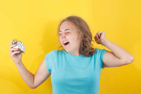 Portrait of shocked girl holding round clock isolated on yellow wall background in studio. People sincere emotions, lifestyle concept. Mock up copy spaceの写真素材