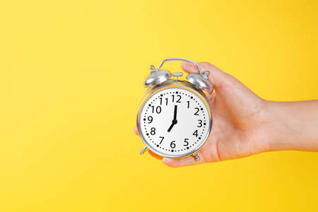 Silver vintage alarm clock in hand on yellow backgroundの写真素材