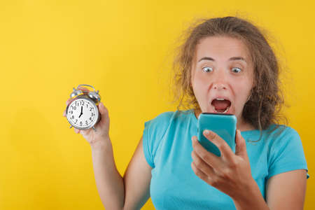 Portrait of shocked girl holding round clock isolated on yellow wall background in studio. People sincere emotions, lifestyle concept. Mock up copy spaceの写真素材