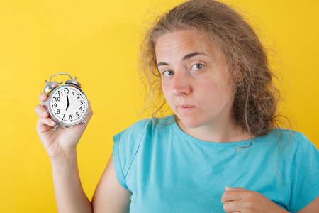 Portrait of shocked girl holding round clock isolated on yellow wall background in studio. People...