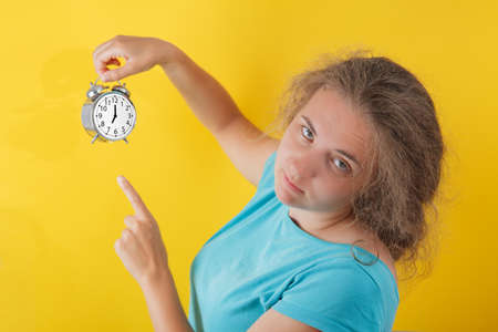 Portrait of shocked girl holding round clock isolated on yellow wall background in studio. People sincere emotions, lifestyle concept. Mock up copy spaceの写真素材