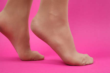 Legs of young caucasian woman in black tights on pink backgroundの写真素材