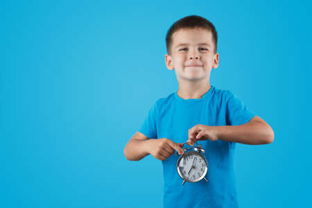 kid boy holding clock alarm, copy space. Time for school. Little student overslept.
