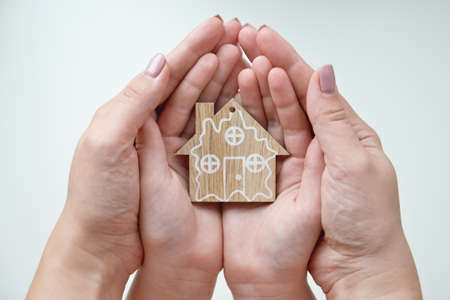 A woman and child are holding a wooden house in their hands. Mom and daughter holds house figurine. New house for the young family concept.の写真素材