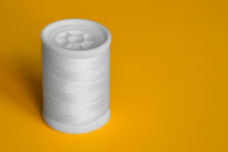 Reel of white sewing threads on yellow background. Copy space, close-up.