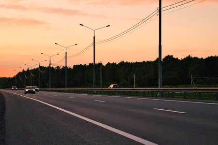 Cars riding on the evening road. Traveling in golden sunset. Highway road landscape.の写真素材