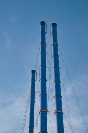 Group of metal chimneys of small local power station or heating boiler against blue sky. Air pollution.の写真素材