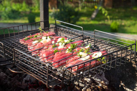 Closeup photo of fresh beef meat with rosemary and garlic on a wire rack. Steaks barbecue on a brazier with natural smoke. Outdoor cooking concept.の写真素材