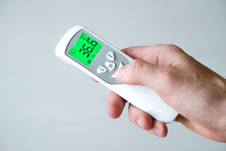 Hand holding contactless thermometer, showing temperature 36.6 degrees by Celsius on white background. Temperature measurement.の写真素材