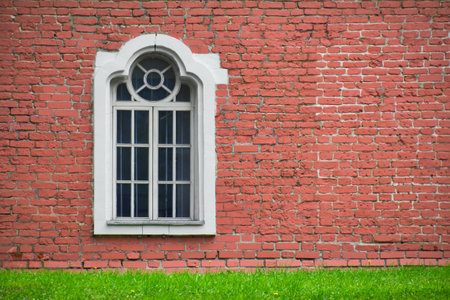 Brick wall with only one window house front. Facade of old building and green meadow. Exterior of ancient house.の写真素材