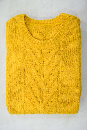 Folded yellow sweater on white background. Casual clothes concept.