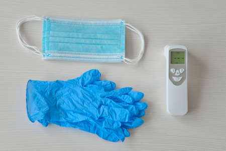 Medical protective mask, rubber gloves and thermometer lie on a white background.