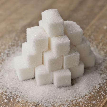 Lump sugar stacked in pyramid on wooden table. Sugar scattered on wooden surface.の写真素材