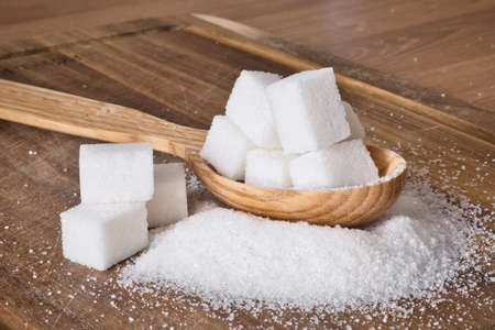 The wooden spoon full of sugar cubes with granulated sugar around on wooden background.の写真素材
