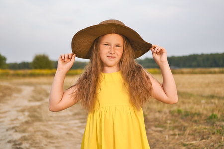 Cute little girl in yellow dress and hat walks in a field. Portrait of the beautiful girl with long hair.の写真素材