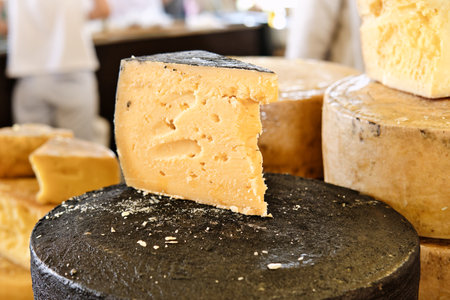 Piece of hard parmesan cheese on the counter of the food market. Head of cheese and cut piece.