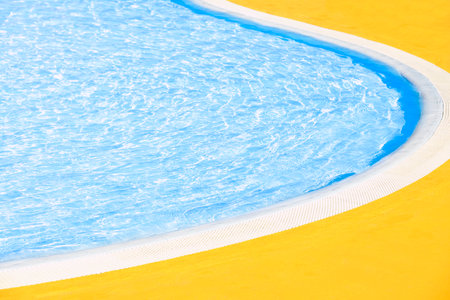 Outdoor swimming pool edge with curved border in sunny summer day. Clear blue water and yellow floor.の写真素材
