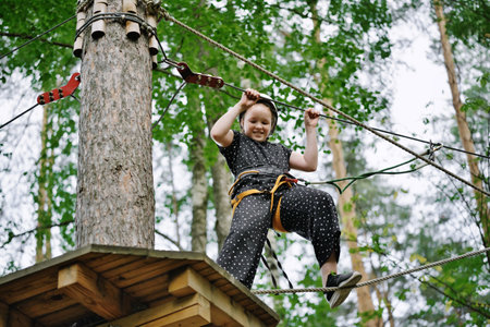 Girl climbs and having fun at outdoor adventure rope park. Active childhood, healthy lifestyle, playing outdoors.の写真素材