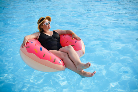 Beautiful white European woman in black swimsuit wear hat and sunglasses relaxing in swimming pool...