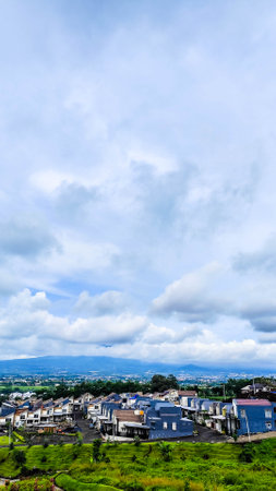 A charming suburban neighborhood with neatly arranged modern houses, set against the backdrop of a majestic mountain partially covered by cloudsの写真素材