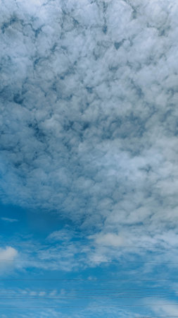 A scenic view of a bright blue sky filled with textured, scattered white cloudsの写真素材