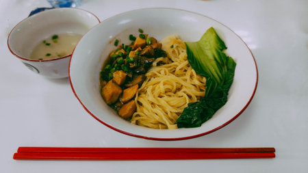 a bowl of noodles with chicken and vegetables served with separate brothの写真素材