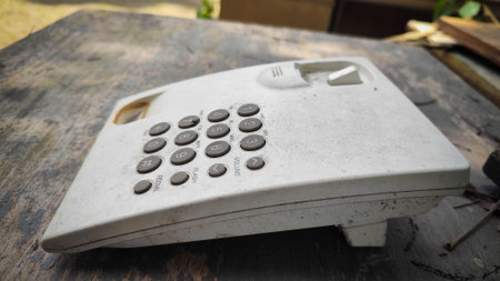 An old, white landline phone covered in dust and debris lies on a weathered wooden surface