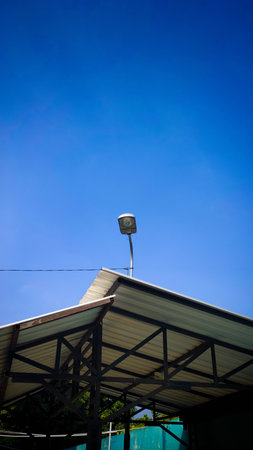A street lamp stands prominently above a corrugated metal roof, silhouetted against a bright blue...