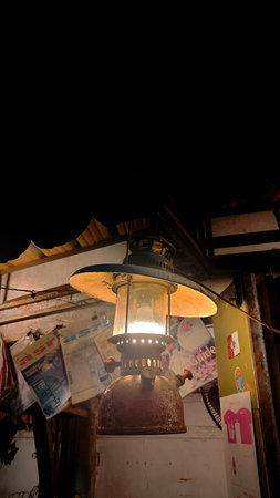 A close-up, low-angle shot of a vintage, rusty kerosene lantern hanging and glowing against a dark...
