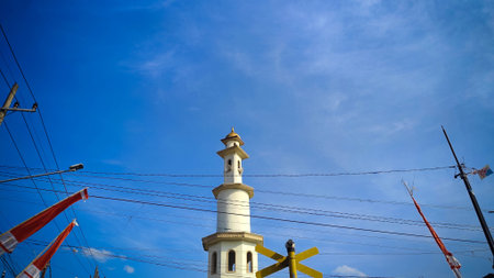 White tiered minaret beneath cloudy sky with many intersecting electrical wires and red flagsの写真素材