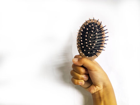 A close up shot of a hand firmly gripping the handle of a brown hair brush.