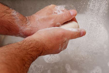 man washing hands with soap in sink with running water