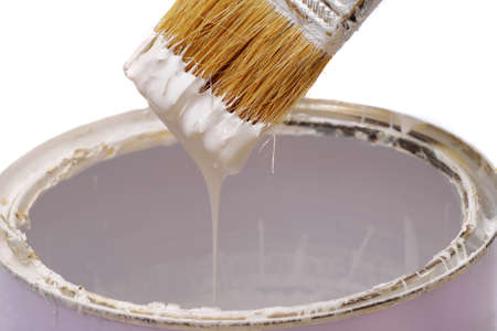closeup of white paint dripping from the brush into a tin