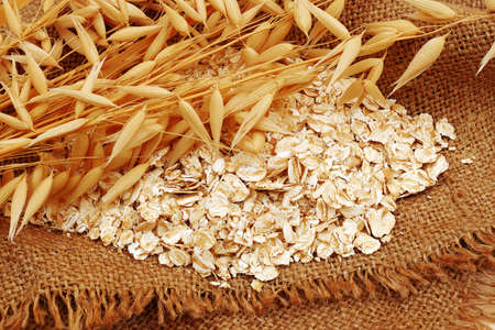 ripe oat ears and pile of oat rolled cereals on sackclothの写真素材