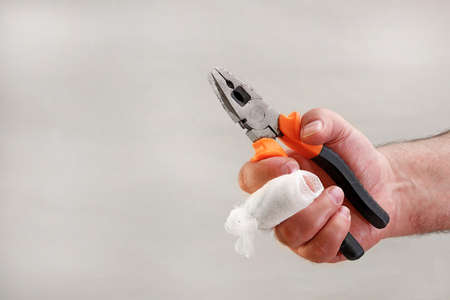 hand with injured finger wrapped with gauze bandage holding pliers with copy space