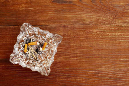 top view of cigarette butts in a glass ashtray on a wooden background with copy spaceの写真素材