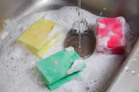 three colorful sponges in kitchen sink under running waterの写真素材
