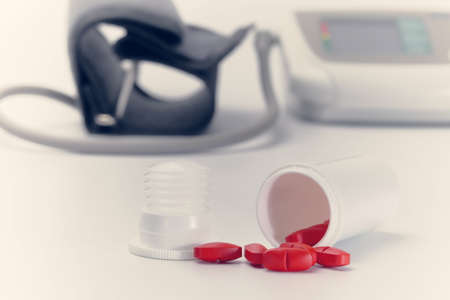 red pills scattered from plastic jar in front of blood pressure monitor, tonedの写真素材
