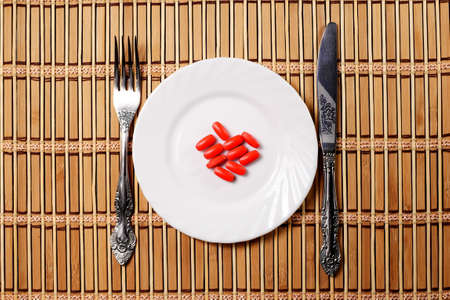 red pills on white plate with fork and knife on table, top viewの写真素材