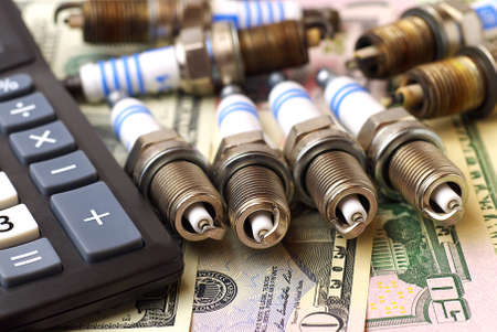 new and used spark plugs and calculator on dollar banknotesの写真素材