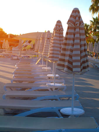 folded umbrellas and sunbeds under sunlight in early morning