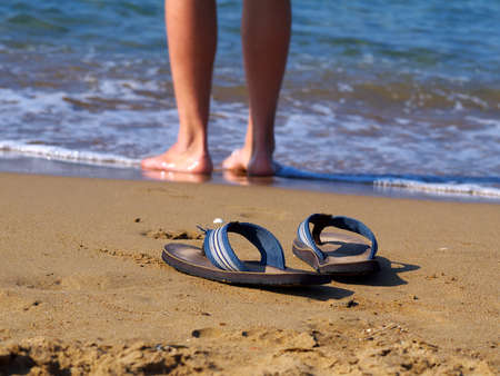 flippers on sand and man walking in water in background,の写真素材