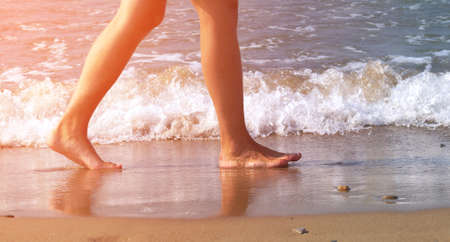 man's feet walking barefoot on beach by water edge, toned, sunlight effectの写真素材