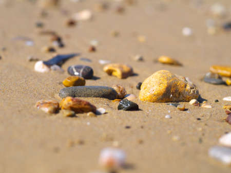 pebble stones on sand on a beach, closeup, shallow depth of fieldの写真素材